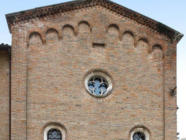 Primo piano di una facciata in mattoni con una finestra decorativa rotonda e piccole aperture ad arco, calde tonalità brune
