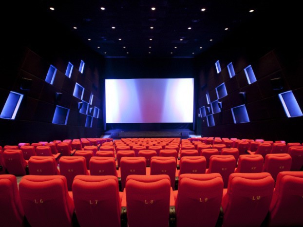 Empty cinema auditorium with rows of red seats facing a large blank screen, dark red and black tones, calm anticipatory atmosphere
